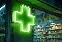 El Día Mundial del Farmacéutico 2026 empodera al farmacéutico Bright green neon cross shining on the exterior of a pharmacy at night, indicating a medical establishment providing medicines and healthcare services