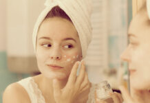 Crema Base DIY: la base ideal para crear cosmética personalizada Woman applying mask moisturizing skin cream on face looking in bathroom mirror. Girl taking care of her complexion layering moisturizer. Skincare spa treatment.