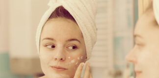 Crema Base DIY: la base ideal para crear cosmética personalizada Woman applying mask moisturizing skin cream on face looking in bathroom mirror. Girl taking care of her complexion layering moisturizer. Skincare spa treatment.