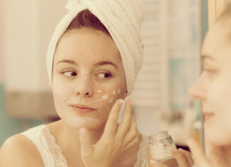 Crema Base DIY: la base ideal para crear cosmética personalizada Woman applying mask moisturizing skin cream on face looking in bathroom mirror. Girl taking care of her complexion layering moisturizer. Skincare spa treatment.