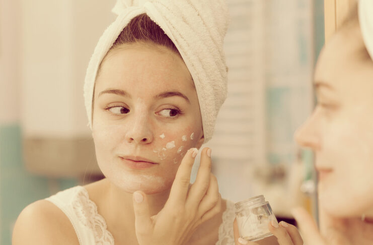 Crema Base DIY: la base ideal para crear cosmética personalizada Woman applying mask moisturizing skin cream on face looking in bathroom mirror. Girl taking care of her complexion layering moisturizer. Skincare spa treatment.